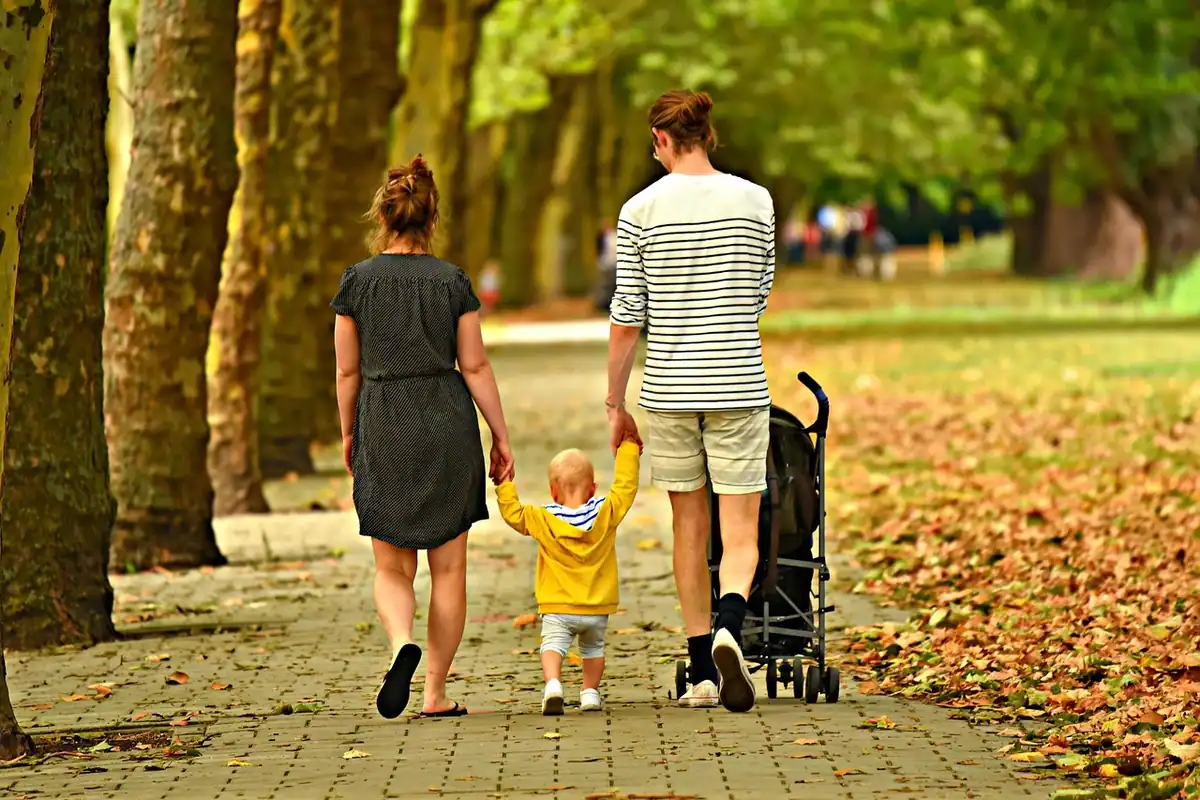 Adulți și un copil mic se plimbă împreună printr-un parc acoperit de frunze toamna