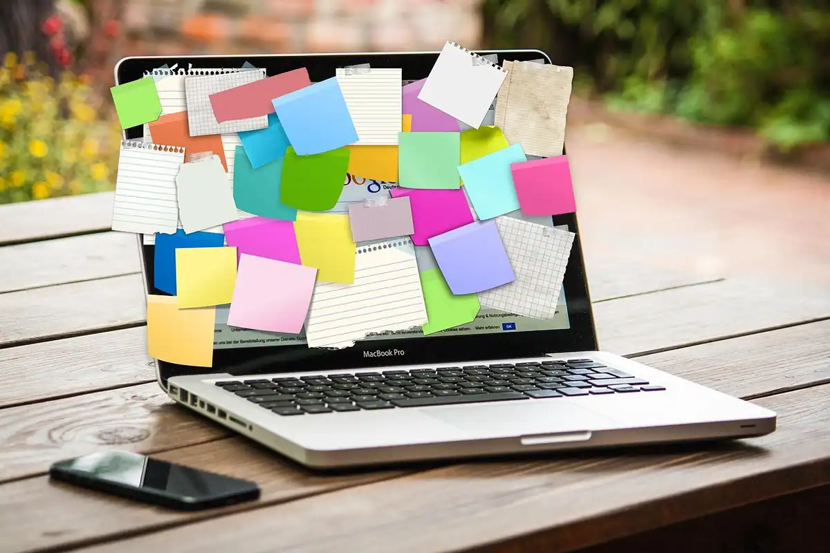 Laptop acoperit cu notițe adezive colorate pe o masă de lemn, cu telefonul alături