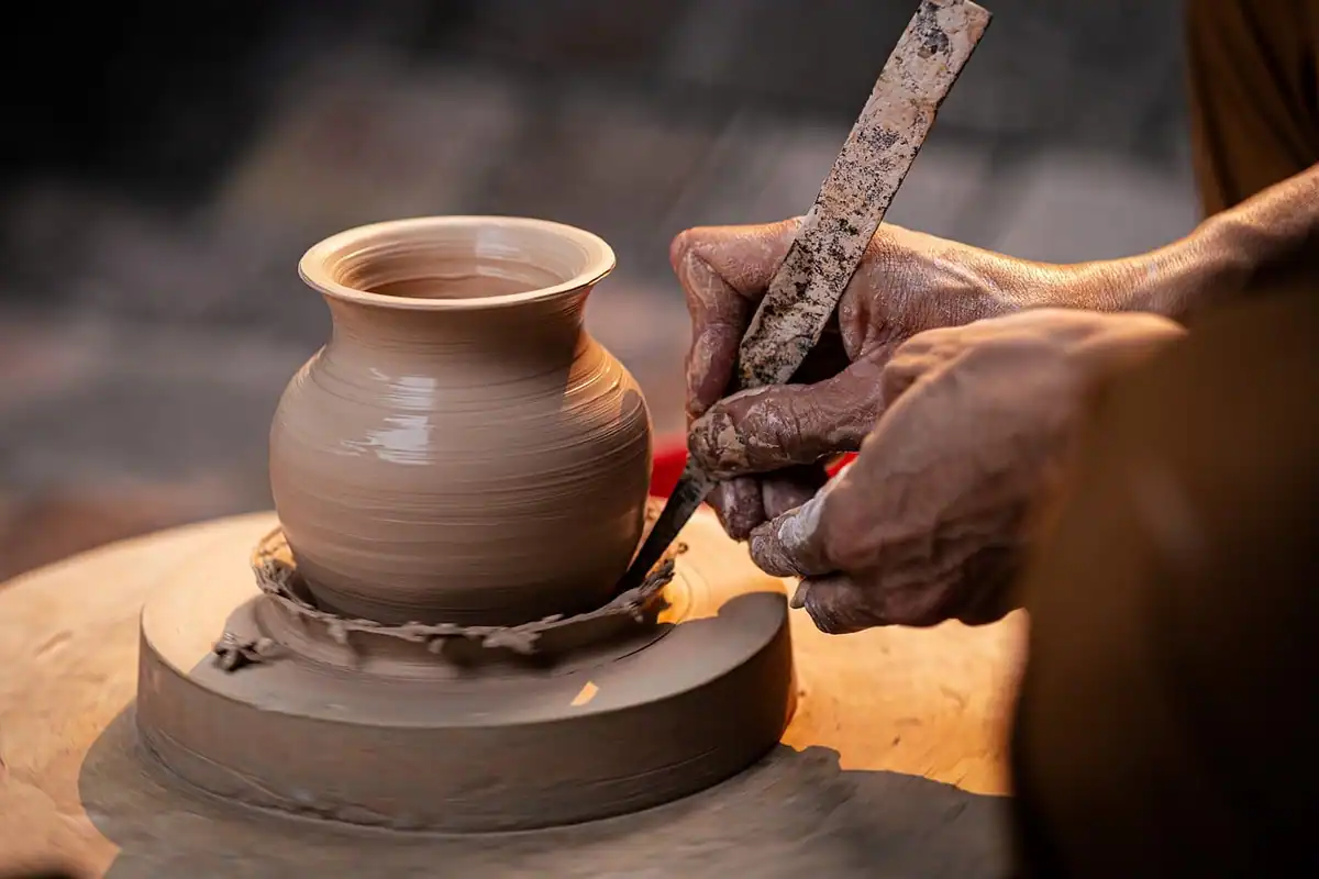 Mâini care modelează o oală de lut pe roata olarului, la un atelier de ceramică