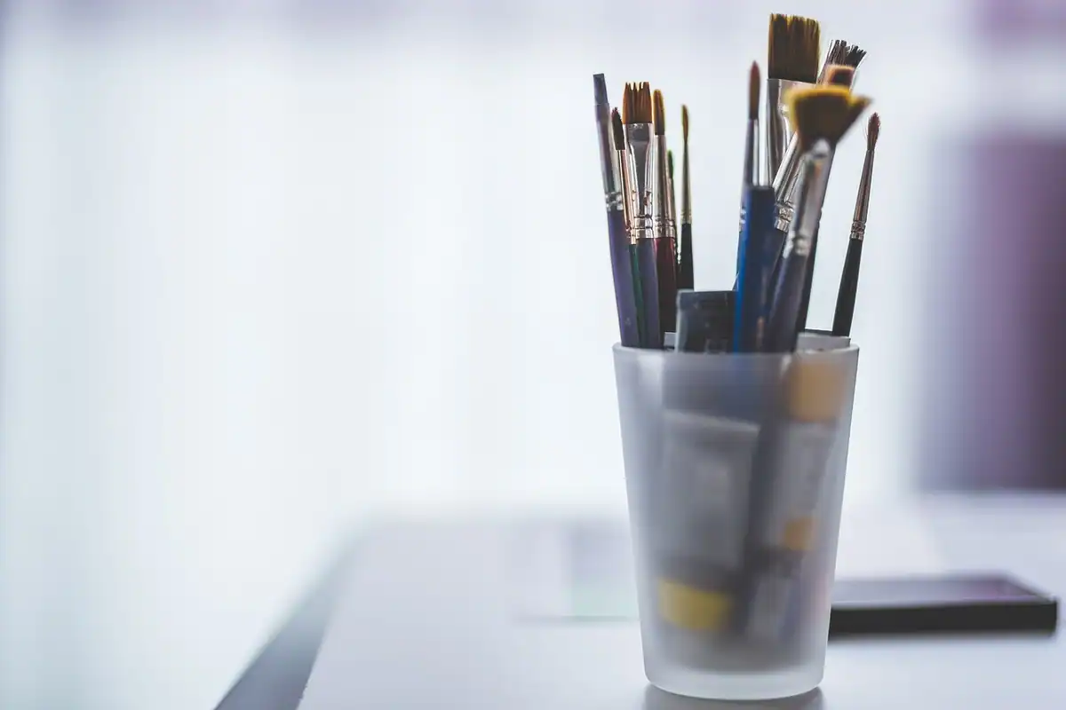 Pensule de pictură într-un pahar transparent, pe o masă luminoasă, pentru proiecte creative