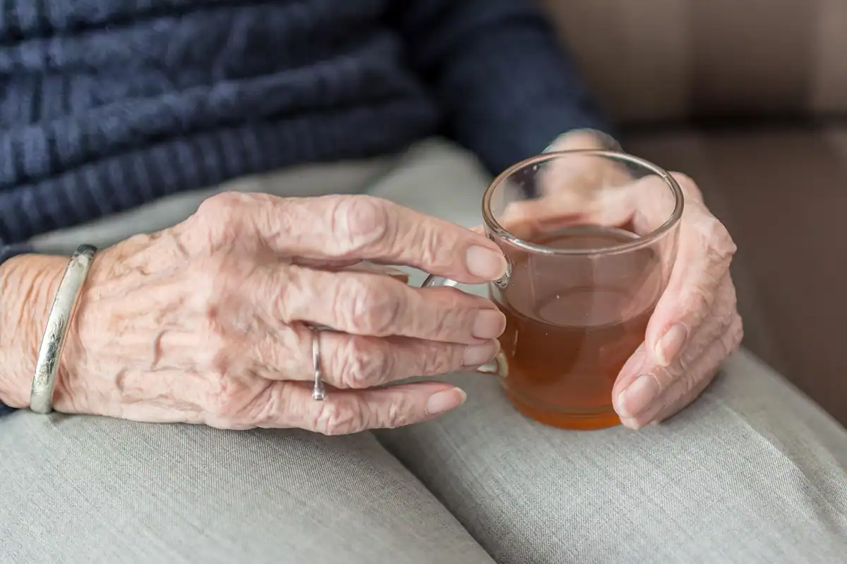 Mâinile unei femei în vârstă care ține un pahar cu ceai cald