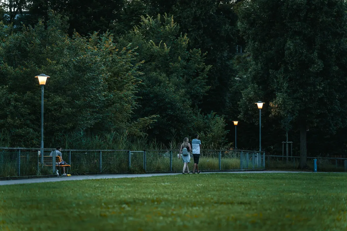 Doi oameni se plimbă seara printr-un parc, pe lângă felinare aprinse